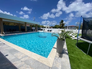 Relax by the clear pool surrounded by a deck, lounge chairs, and a shaded seating area.