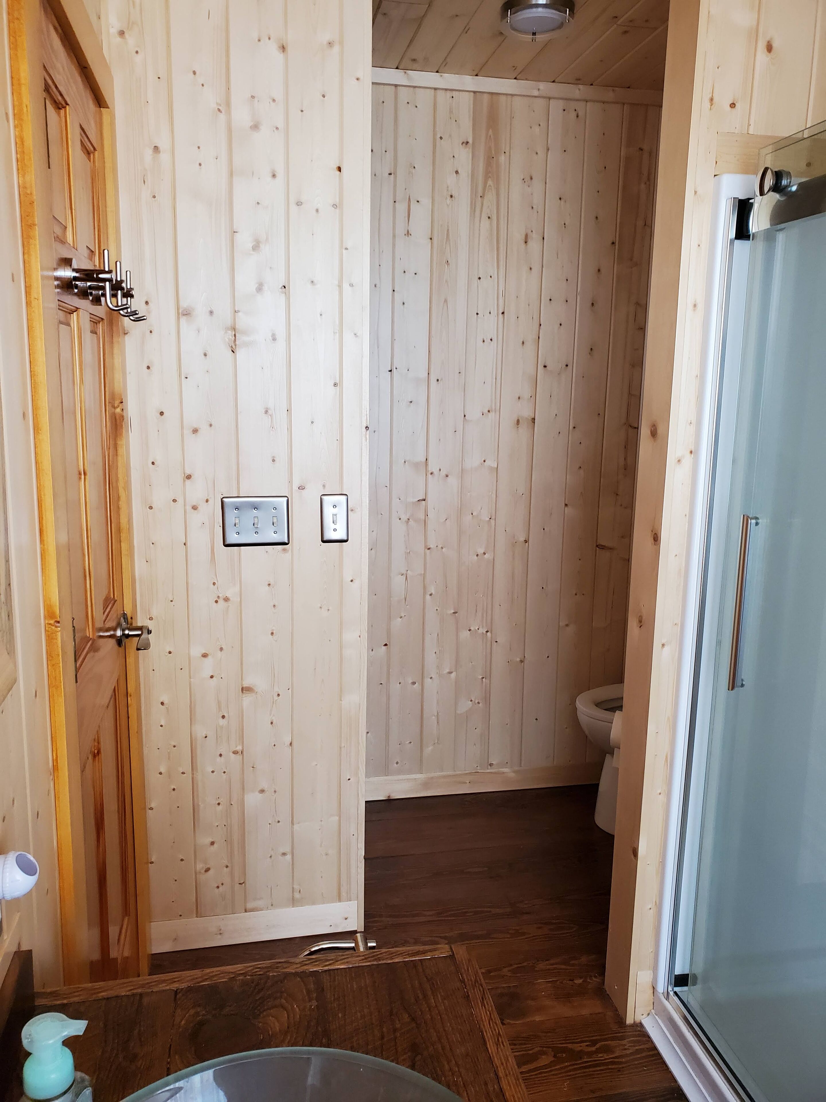 Un baño con paneles de madera, un inodoro, cabina de ducha y lavamanos.