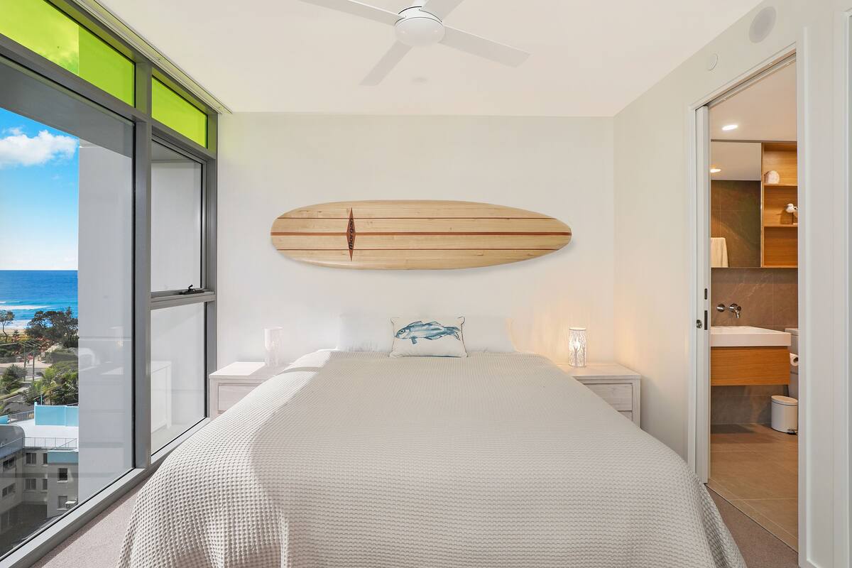 Un dormitorio con una cama grande, ventilador de techo, vista al océano y baño de diseño moderno.