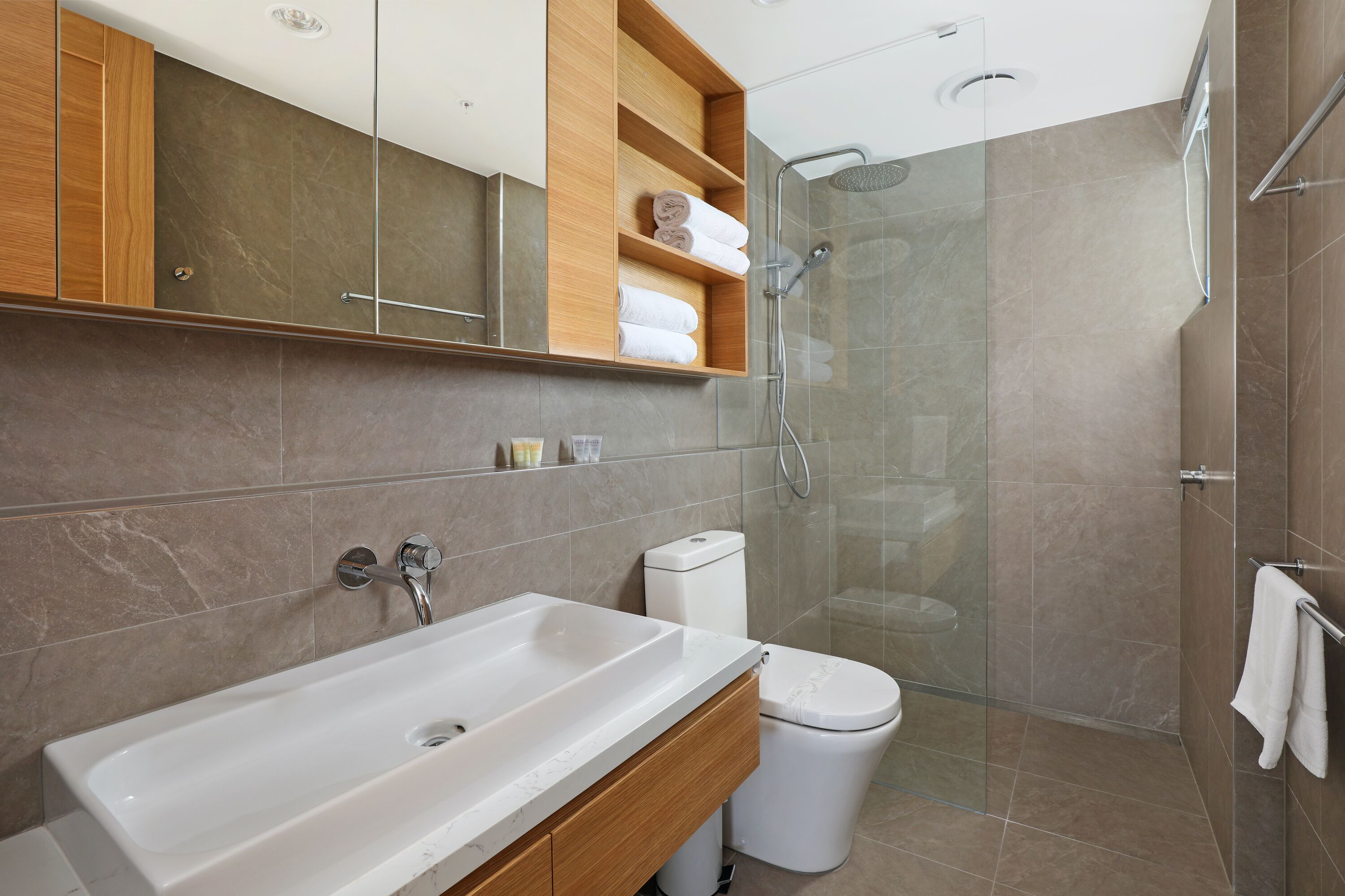 A modern bathroom with a large white sink, wooden vanity, a glass shower enclosure, and a toilet.