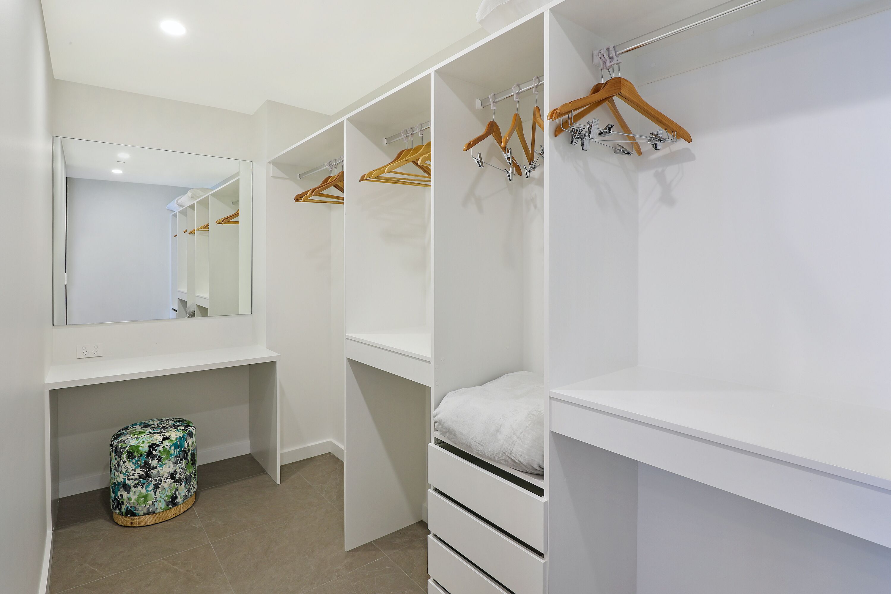 A walk-in closet with white storage units, wooden hangers, and a mirrored wardrobe.