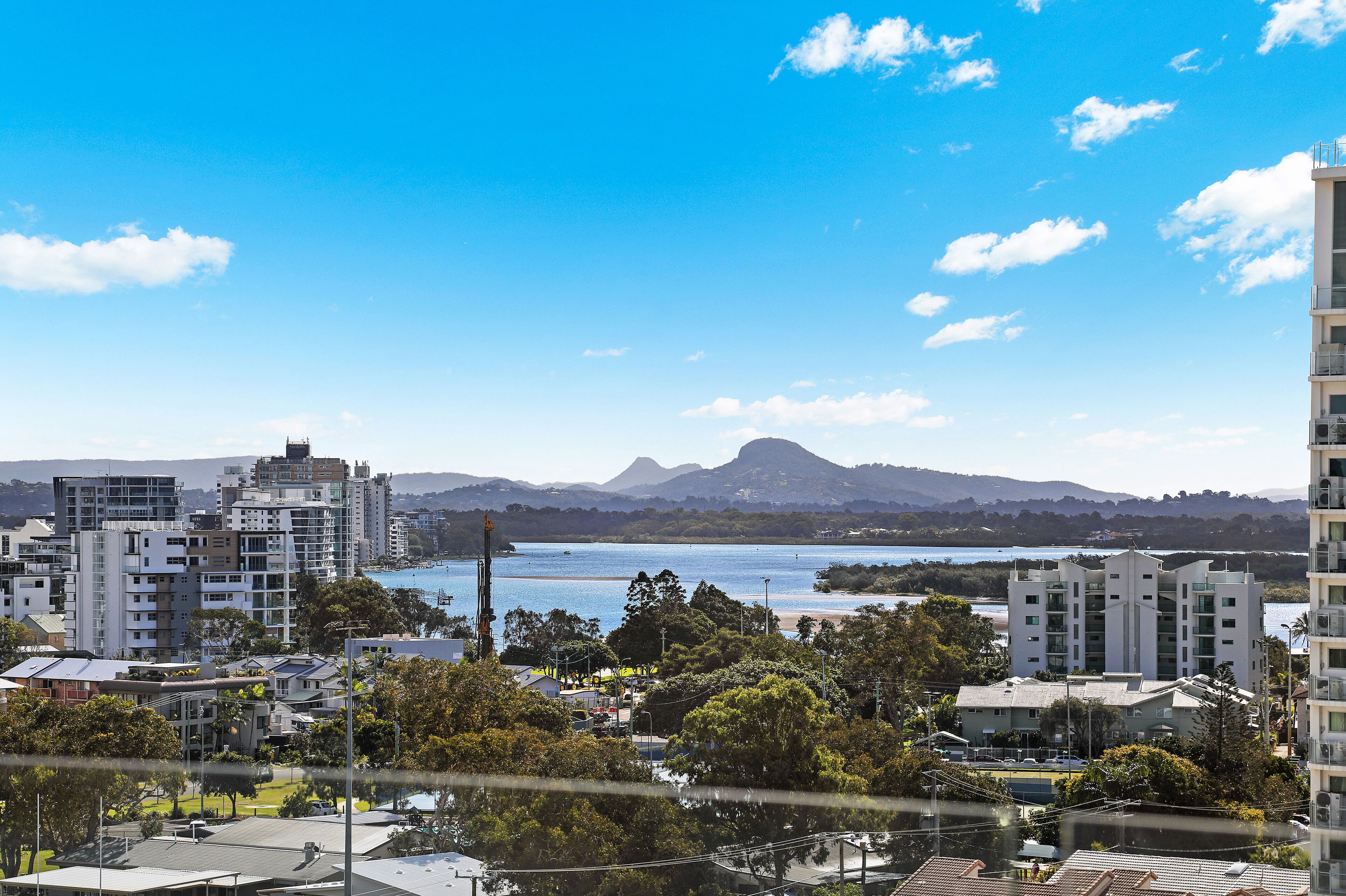 A coastal cityscape with modern buildings, a clear blue sky, and a mountain in the background.