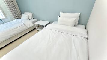 A hotel room with two beds, a small white nightstand, and a window with curtains.