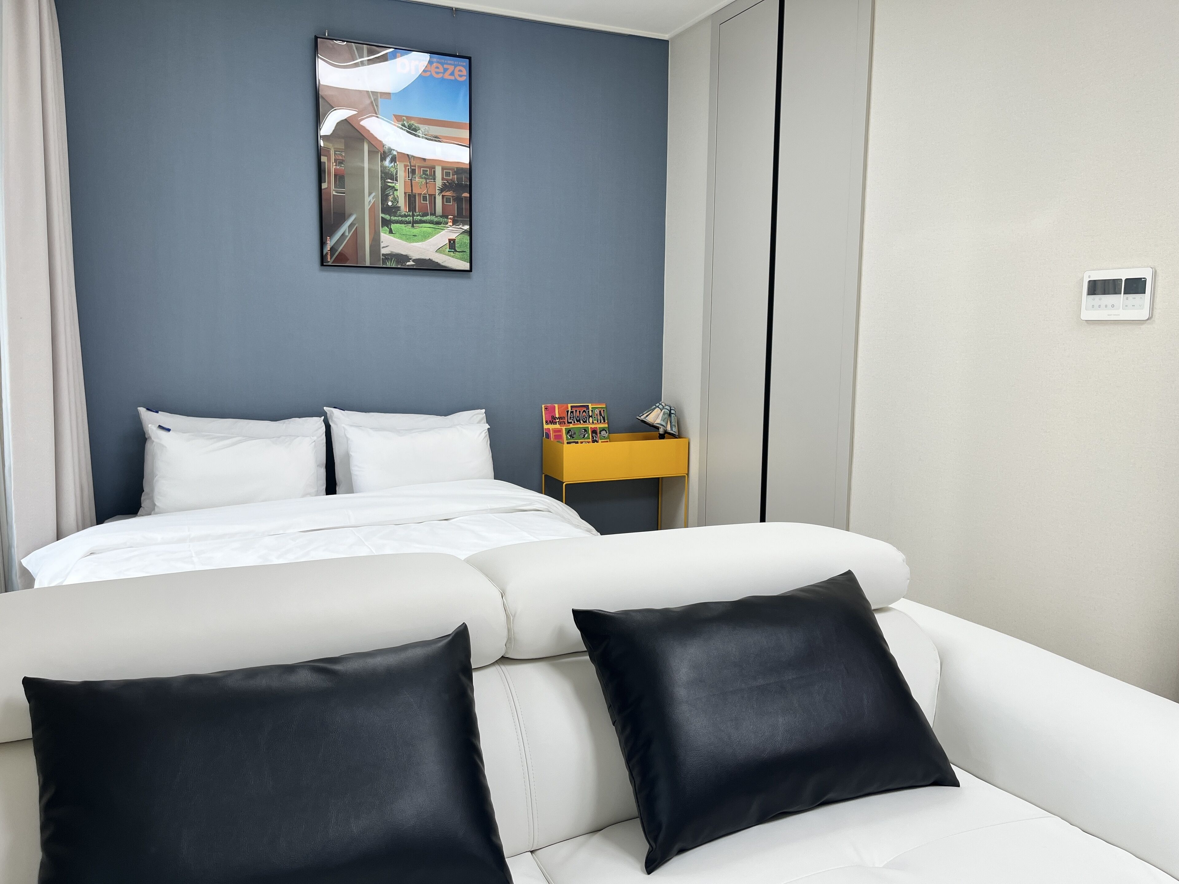 Una habitación de hotel con una cama, un sofá blanco y una pequeña mesita amarilla con una revista.