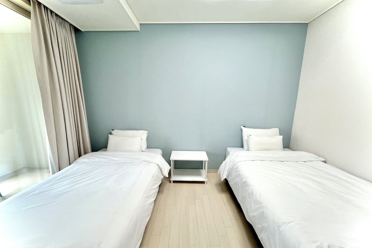 Ein Hotelzimmer mit zwei Einzelbetten, einem kleinen Nachttisch und einem Fenster mit Vorhängen.