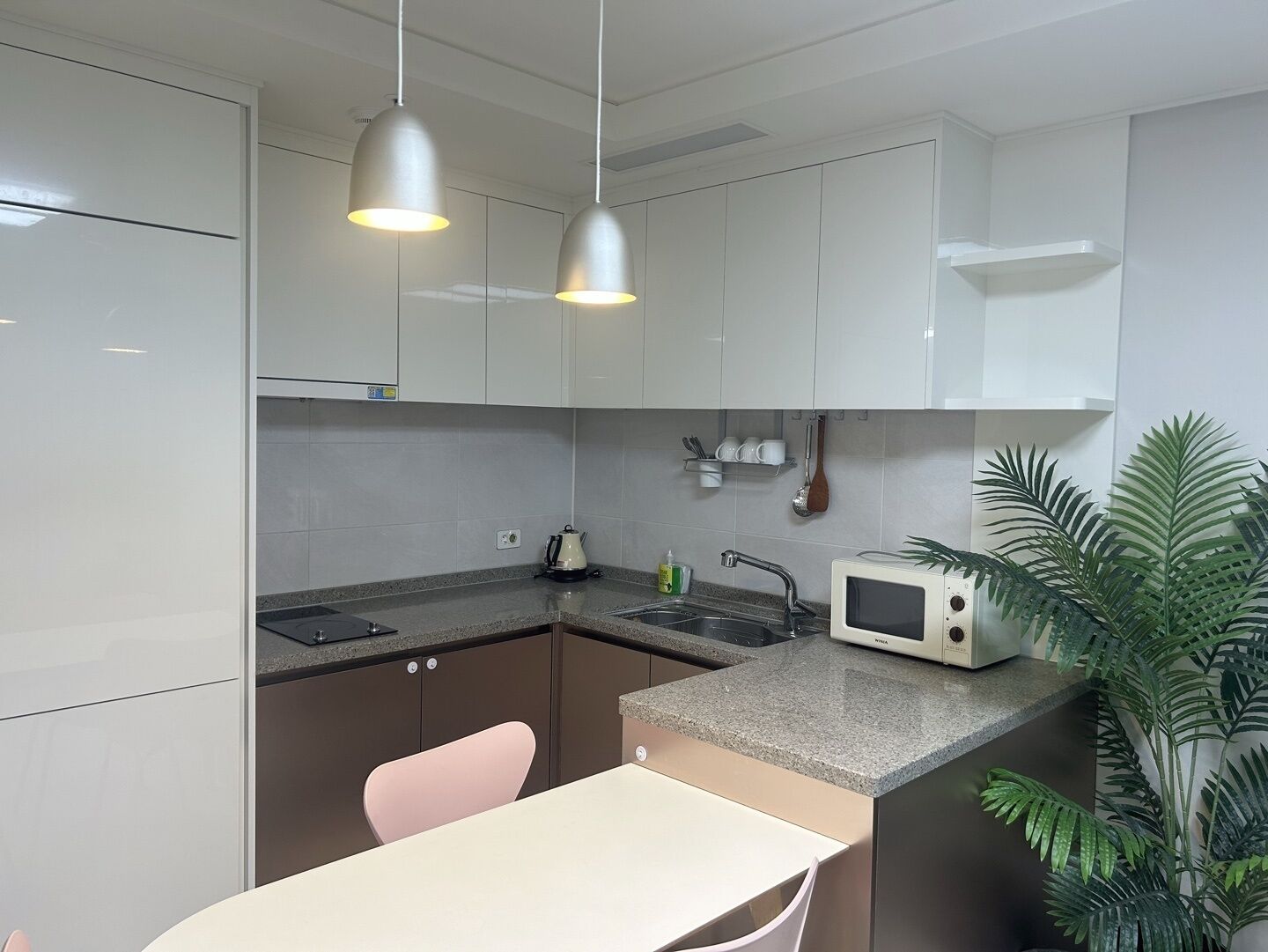 Une cuisine moderne avec des meubles blancs, un plan de travail en granit, un four à micro-ondes, un évier et des luminaires suspendus.