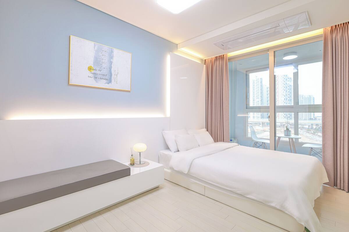 Ein modernes Hotelzimmer mit Bett, Nachttisch und Blick auf die Stadt durch große Fenster.