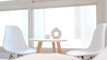 A room with two white chairs, a small round table, and a vase.