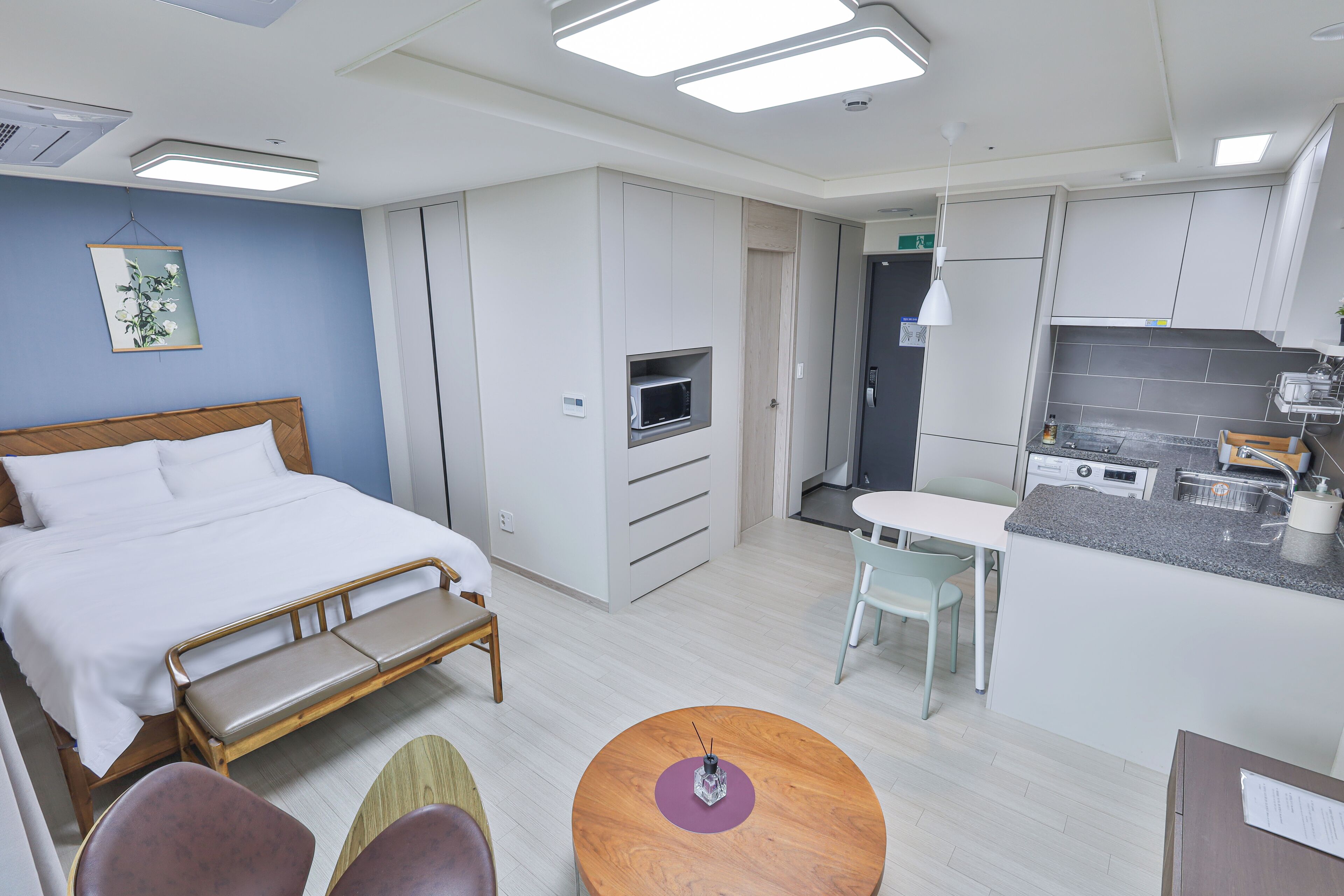 A modern hotel room with a bed, a small kitchenette, a dining area, and a bathroom.