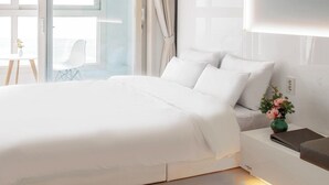 A modern hotel room with a large bed, a small bedside table with a vase of flowers, and a view of the sea through a glass door. - Landmark Stay in Songdo (Incheon)
