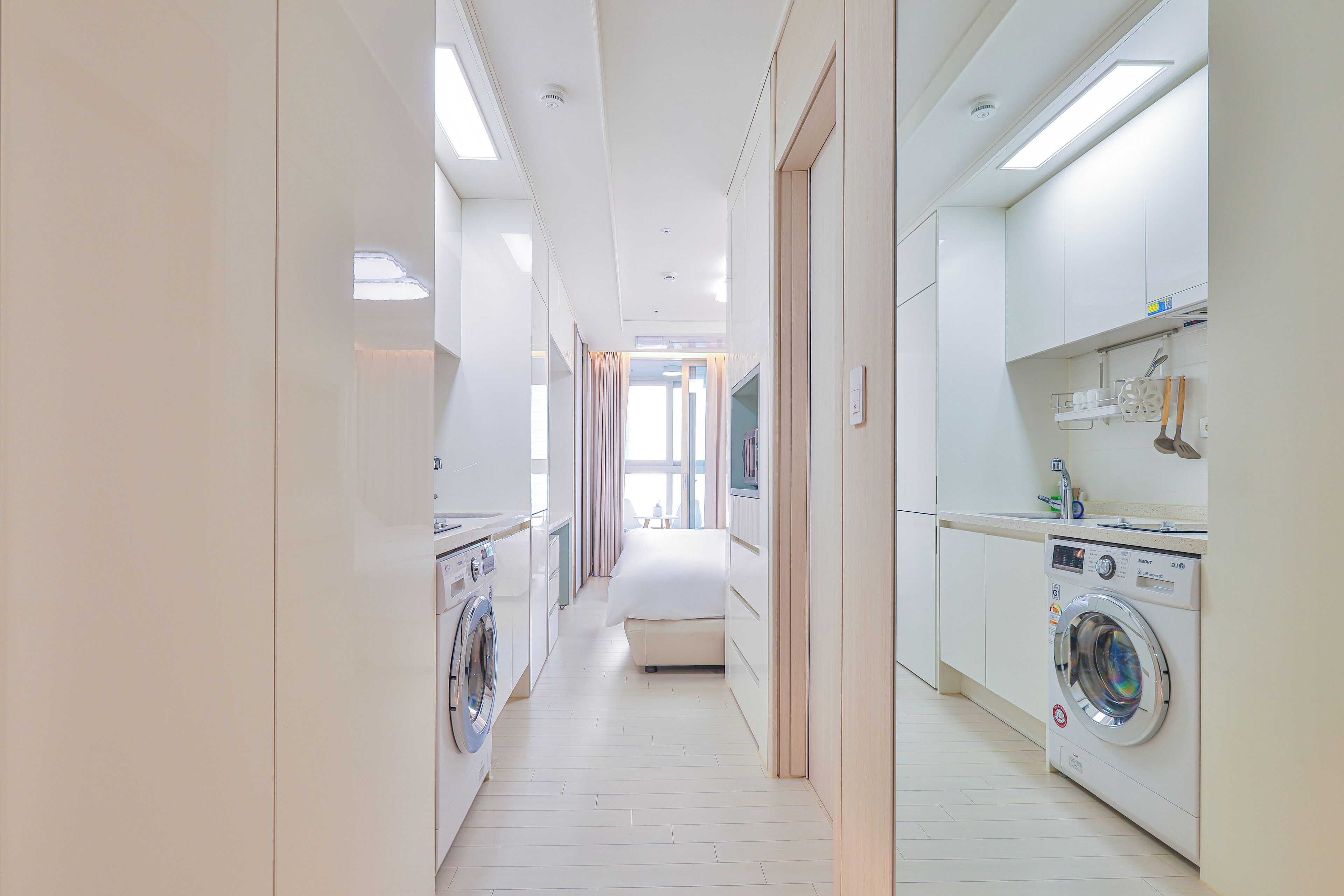 A modern hotel room with a washing machine, a bed, and a bathroom with a sink and mirror.