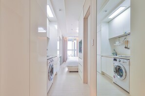 Moderni hotellihuone, jossa on pyykinpesukone, sänky sekä kylpyhuone, jossa on pesuallas ja peili.
