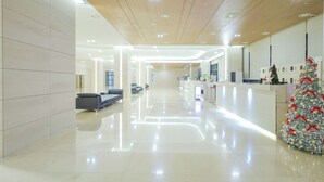 A spacious lobby with a polished floor, a reception desk, and a Christmas tree. - Landmark Stay in Songdo (Incheon)