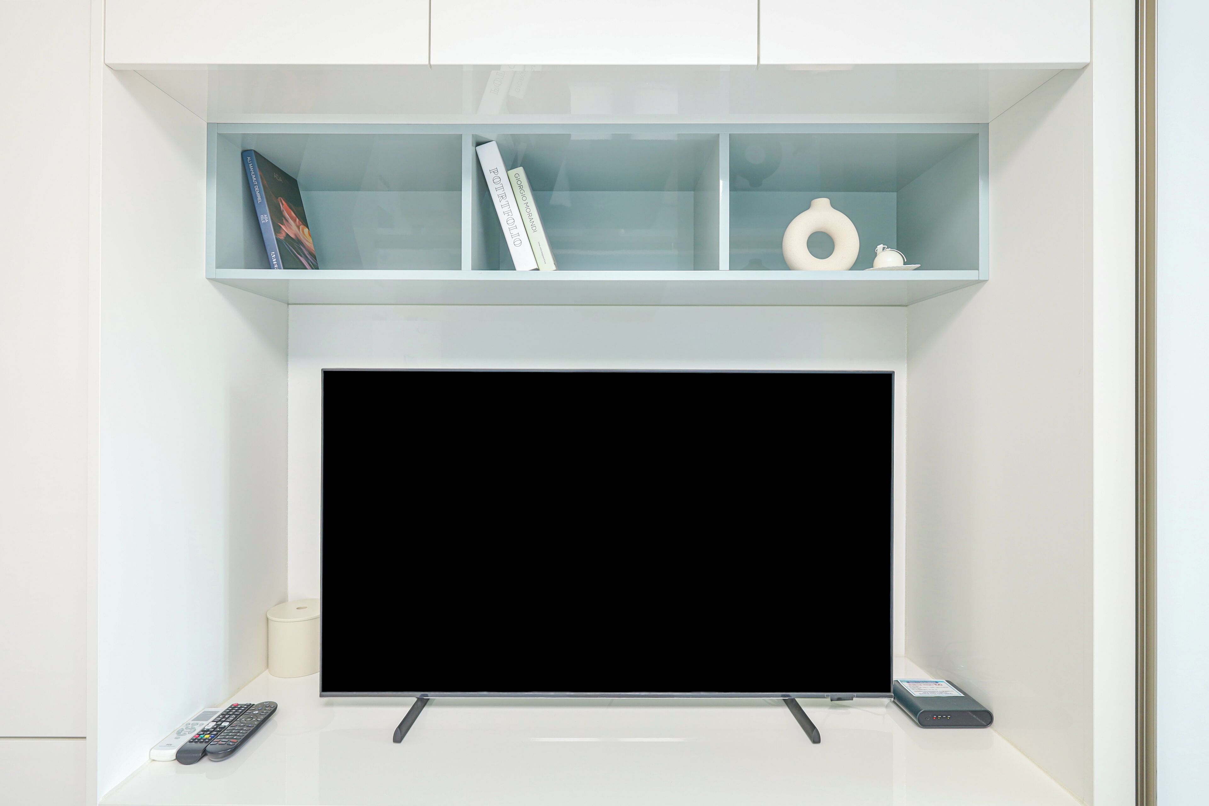 Un salon moderne avec un téléviseur à écran plat, une télécommande et un objet décoratif posé sur l’étagère au-dessus.