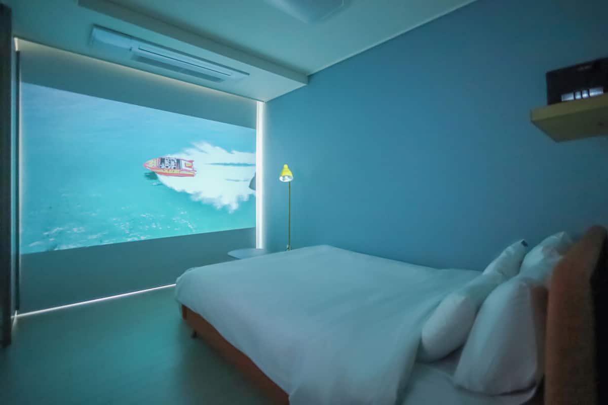 Ein Schlafzimmer mit einem Bett, einem Nachttisch, einer Lampe und einem an der Wand befestigten Regal.
