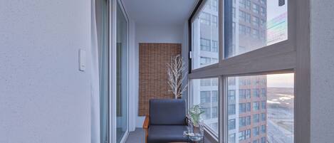 A modern, narrow balcony with a view of a cityscape, a black chair, a small table, and a potted plant.