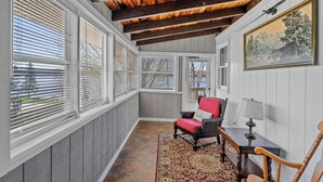 A sunroom with large windows, a red chair, a table, and a painting on the wall.