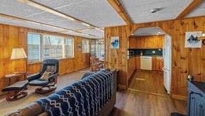 A cabin interior with a living area, wooden walls, a kitchen, and a dining area.