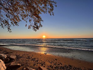 En strand med solnedgang over havet, sten og en gren i forgrunden.
