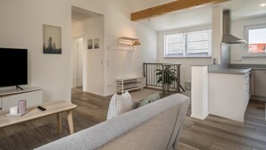 A modern living room with a sofa, TV, and a small table. There is a kitchen area with a stove and cabinets. - Attic Apartment ‘Marla’ with Wi-Fi & Balcony (Eriskirch)