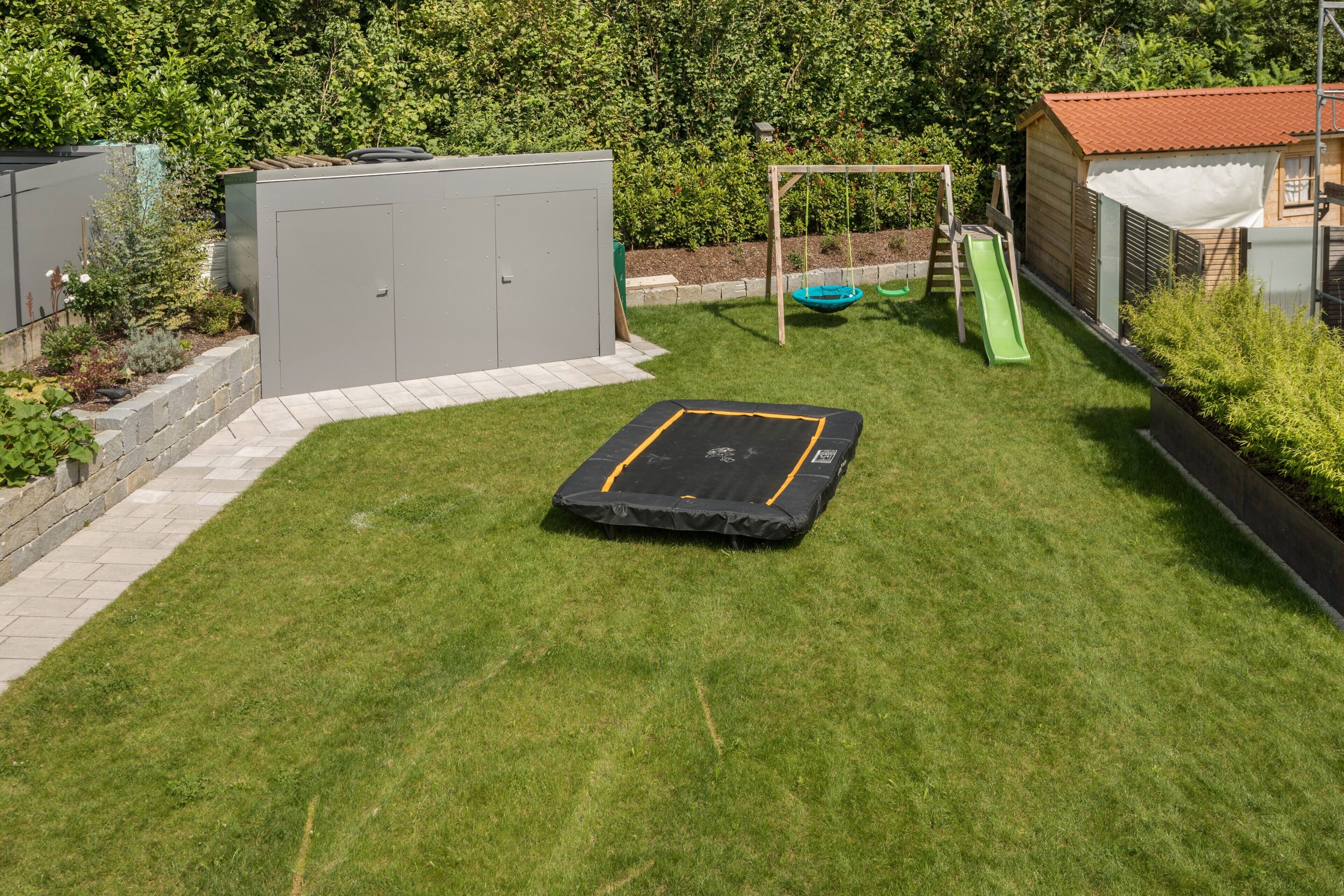 Ein Garten mit Trampolin, Schaukel und Gartenhaus.