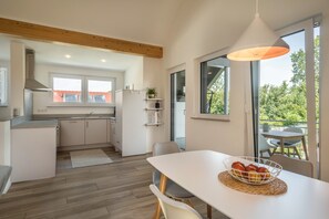 A modern kitchen with a dining area, large windows, and a view of the outdoors.