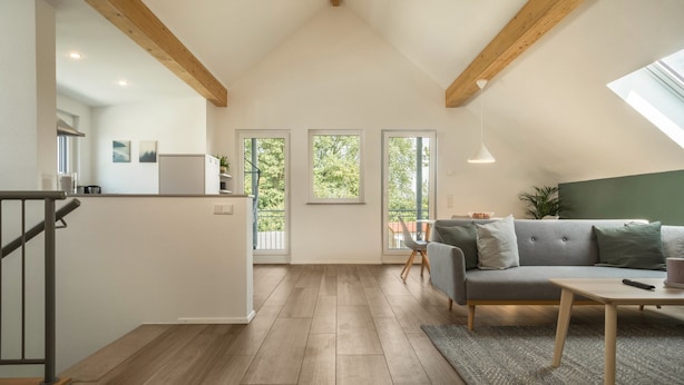 A modern interior with a loft-style ceiling, a grey sofa, a wooden dining table, and a kitchen area. - Attic Apartment ‘Marla’ with Wi-Fi & Balcony (Eriskirch)