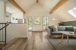 A modern interior with a loft-style ceiling, a grey sofa, a wooden dining table, and a kitchen area. - Attic Apartment ‘Marla’ with Wi-Fi & Balcony (Eriskirch)