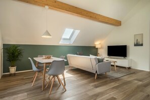 A modern loft-style room with a dining area, sofa, TV, and skylight. - Attic Apartment ‘Marla’ with Wi-Fi & Balcony (Eriskirch)