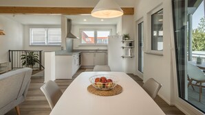 A modern kitchen with white cabinets, a hanging light fixture, and a dining area with a white table and chairs. - Attic Apartment ‘Marla’ with Wi-Fi & Balcony (Eriskirch)