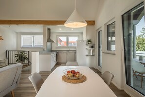 A modern kitchen with white cabinets, a hanging light fixture, and a dining area with a white table and chairs.