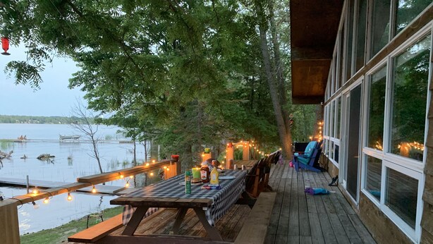 A wooden deck with a picnic table, string lights, and a view of a lake. - Water Access Only Cottage on Georgian Bay (Tay)