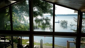 A large window with a view of a lake and dock. Inside, there is a wooden deck with outdoor furniture. - Water Access Only Cottage on Georgian Bay (Tay)