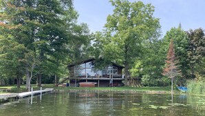 A lakeside cabin with a deck, surrounded by trees and a dock extending into the water. - Water Access Only Cottage on Georgian Bay (Tay)