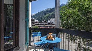 A balcony with a table set for two, a chair, and a view of a mountain and buildings.