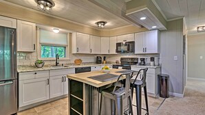 A modern kitchen with white cabinets, stainless steel appliances, and a bar area with stools. - Deck & Gas Grill: Modern East Stroudsburg Home! (East Stroudsburg)
