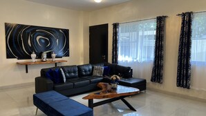 A modern living room with a black leather sofa, a blue ottoman, a wooden coffee table, and a large abstract painting on the wall. - New lovely house at walking distance from beautiful Sosua beach.  (Sosúa)