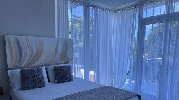 A bedroom with a large bed, white bedding, grey pillows, and a grey quilted blanket. - New lovely house at walking distance from beautiful Sosua beach.  (Sosúa)