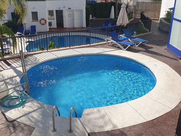 A circular swimming pool with a metal ladder, surrounded by lounge chairs and a tiled deck.