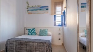 A bedroom with a bed, a window with curtains, a wall-mounted artwork, and a door.