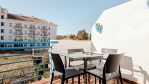 A balcony with a glass table and chairs, a blue railing, and a white wall.