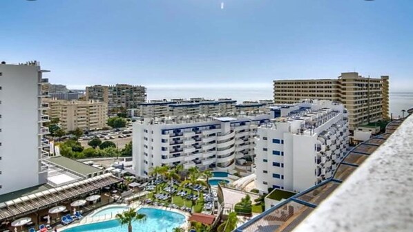 A high-rise hotel with multiple balconies, a swimming pool, and a view of the sea.