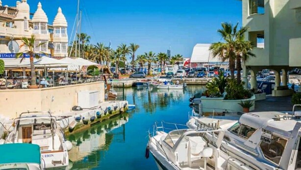 Un port de plaisance avec des bateaux amarrés, un restaurant et un bâtiment à la façade blanche.