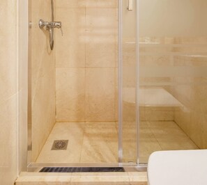 A glass-enclosed shower with a tiled floor and a drain.