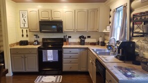 A kitchen with white cabinets, a black stove, a microwave, and a coffee maker.