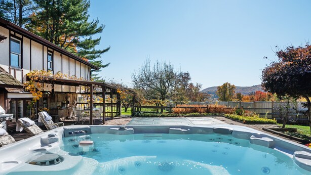 A hot tub in a backyard with a house, trees, and a clear sky.