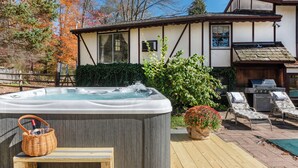 A hot tub with a wicker basket, lounge chairs, and a barbecue grill in a backyard.