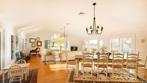 A spacious living room with a dining area, large windows, and a chandelier.