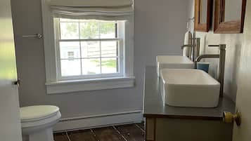 A bathroom with a white toilet, a window with a view, a white sink, and a wooden vanity.