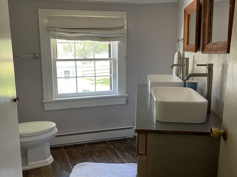 A bathroom with a white toilet, a window with a view, a white sink, and a wooden vanity.